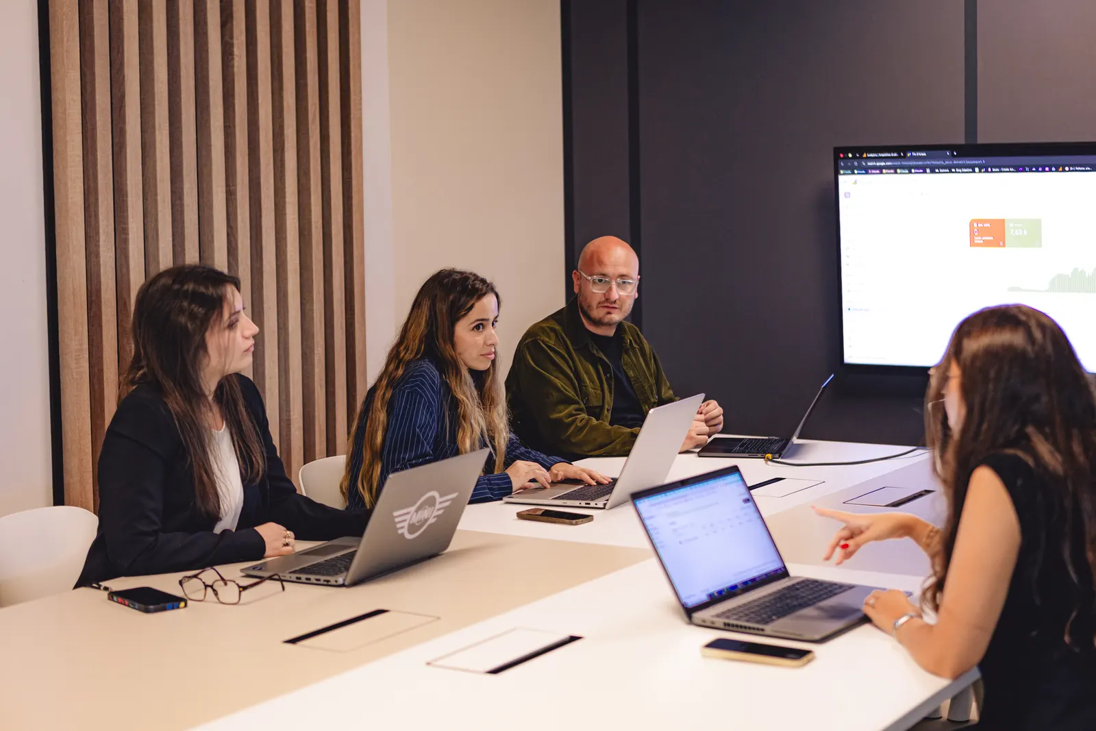 Équipe réunie autour d’une grande table de travail, ordinateurs portables ouverts